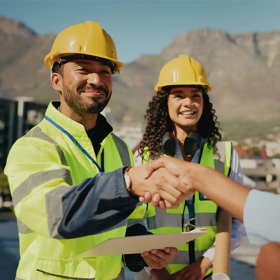 Construction workers shaking hands, smiling outdoors.