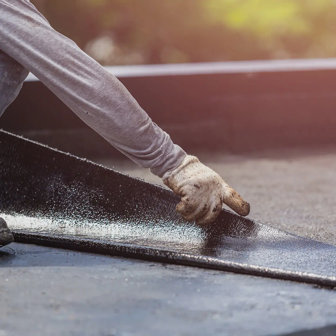 Worker laying roofing material on surface.